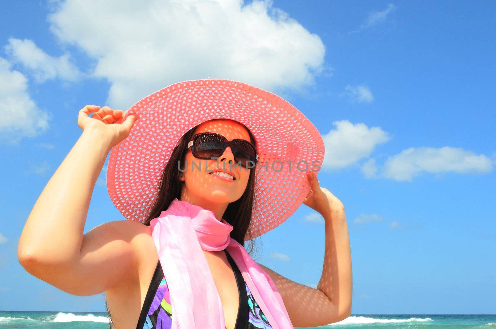 The young woman lifted her head to the sun and keeps the pink hat with both hands