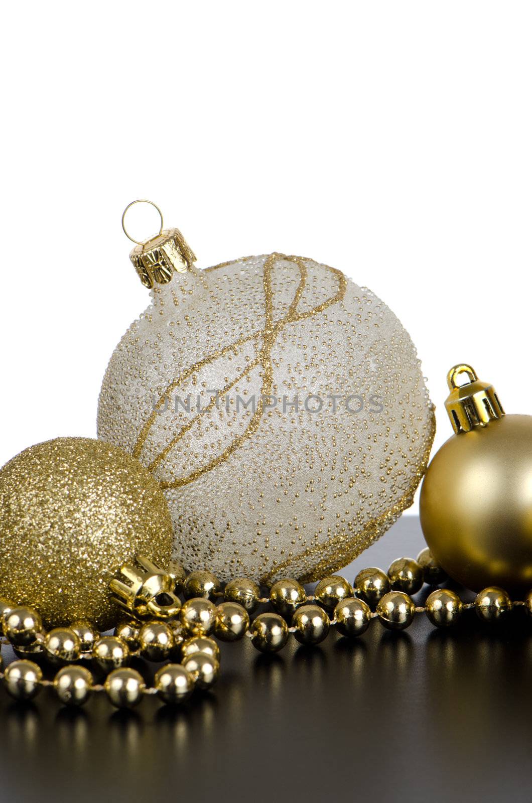 Golden christmas balls with decorations on black surface and white backdrop.