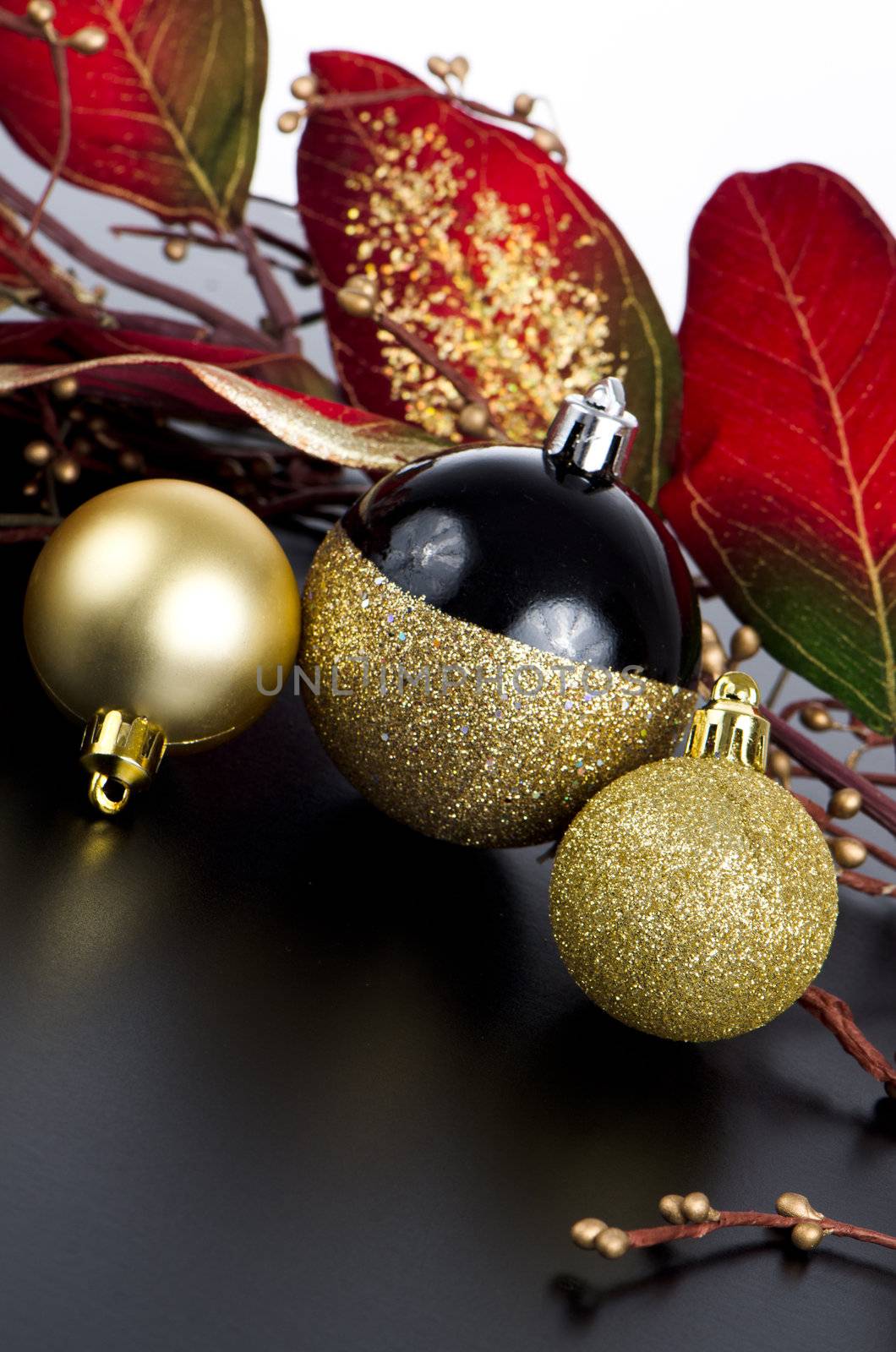 Golden christmas balls with decorations on black surface and white backdrop.