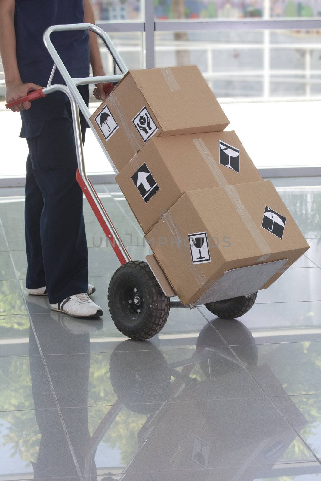 Side view of delivery woman in uniform pushing stack of cardboard boxes on dolly