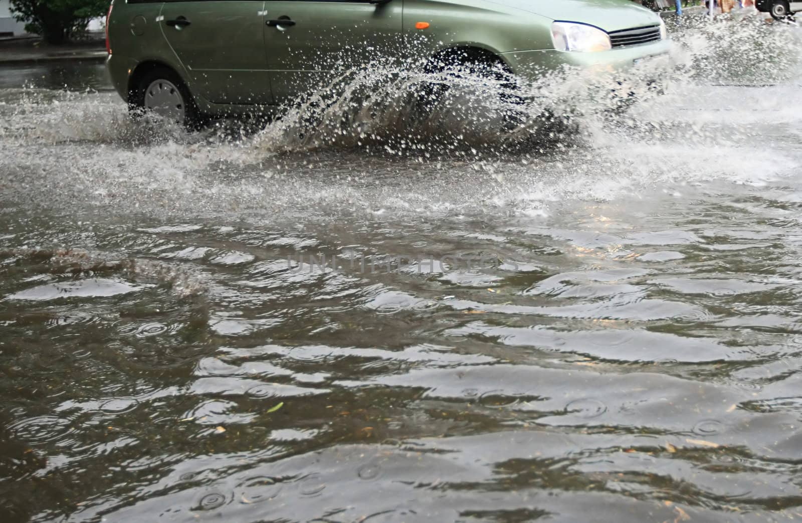 A car splashes through a large puddle on a wet road.