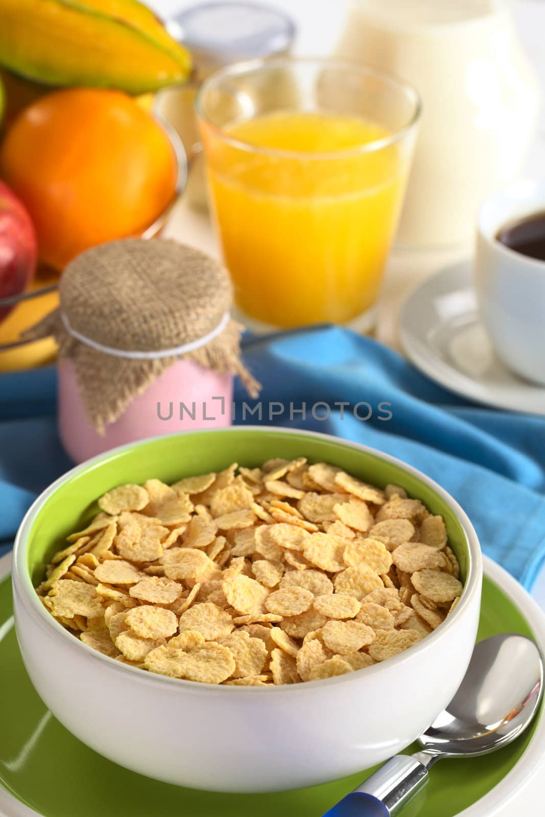 Sweetened corn flakes with yogurt, coffee, orange juice, fresh fruits and milk in the back (Selective Focus, Focus one third into the bowl)