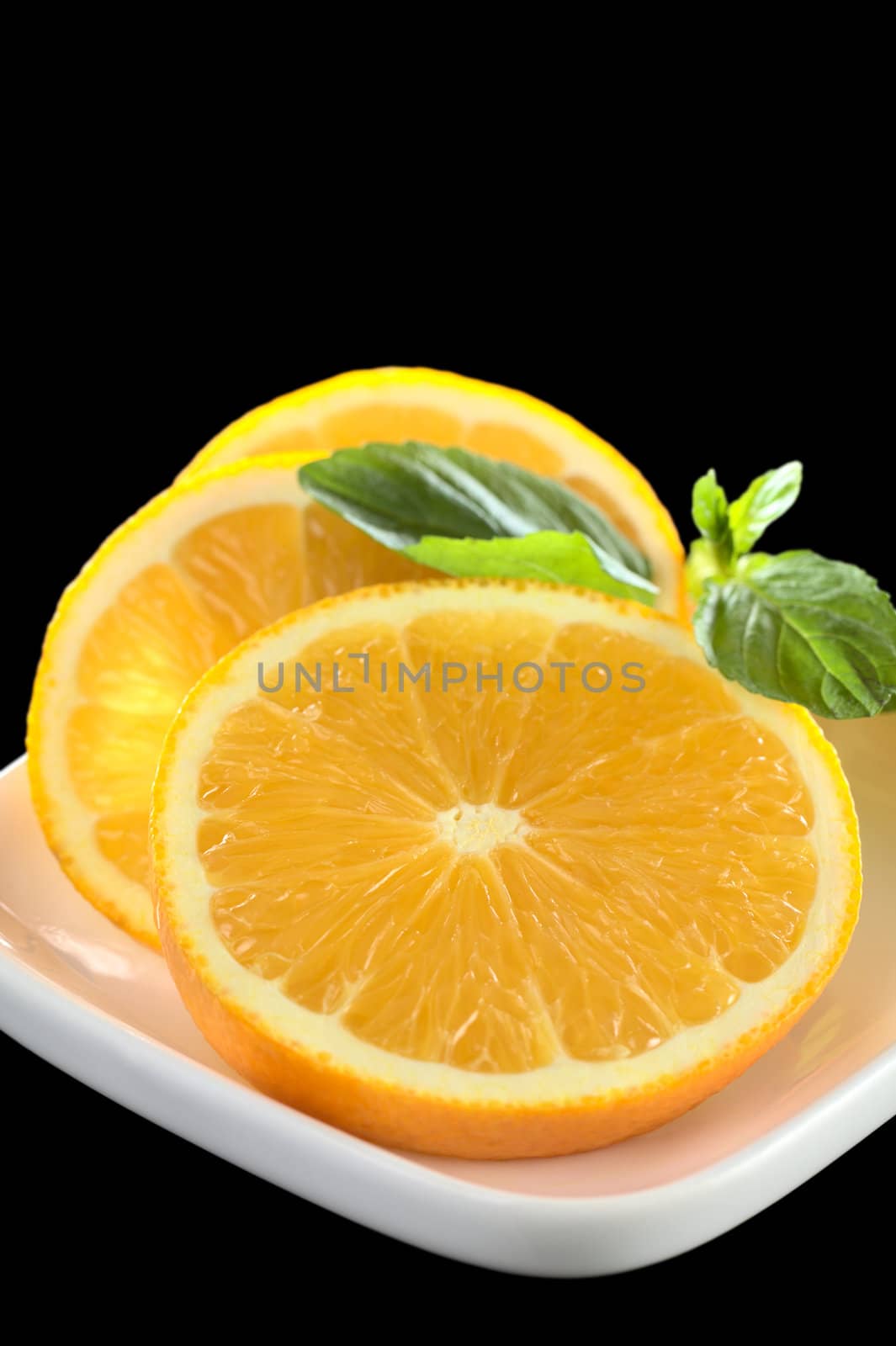 Fresh orange slices served on small plate garnished with a mint leaf photographed on black (Selective Focus, Focus on the middle of the orange slice in the front)