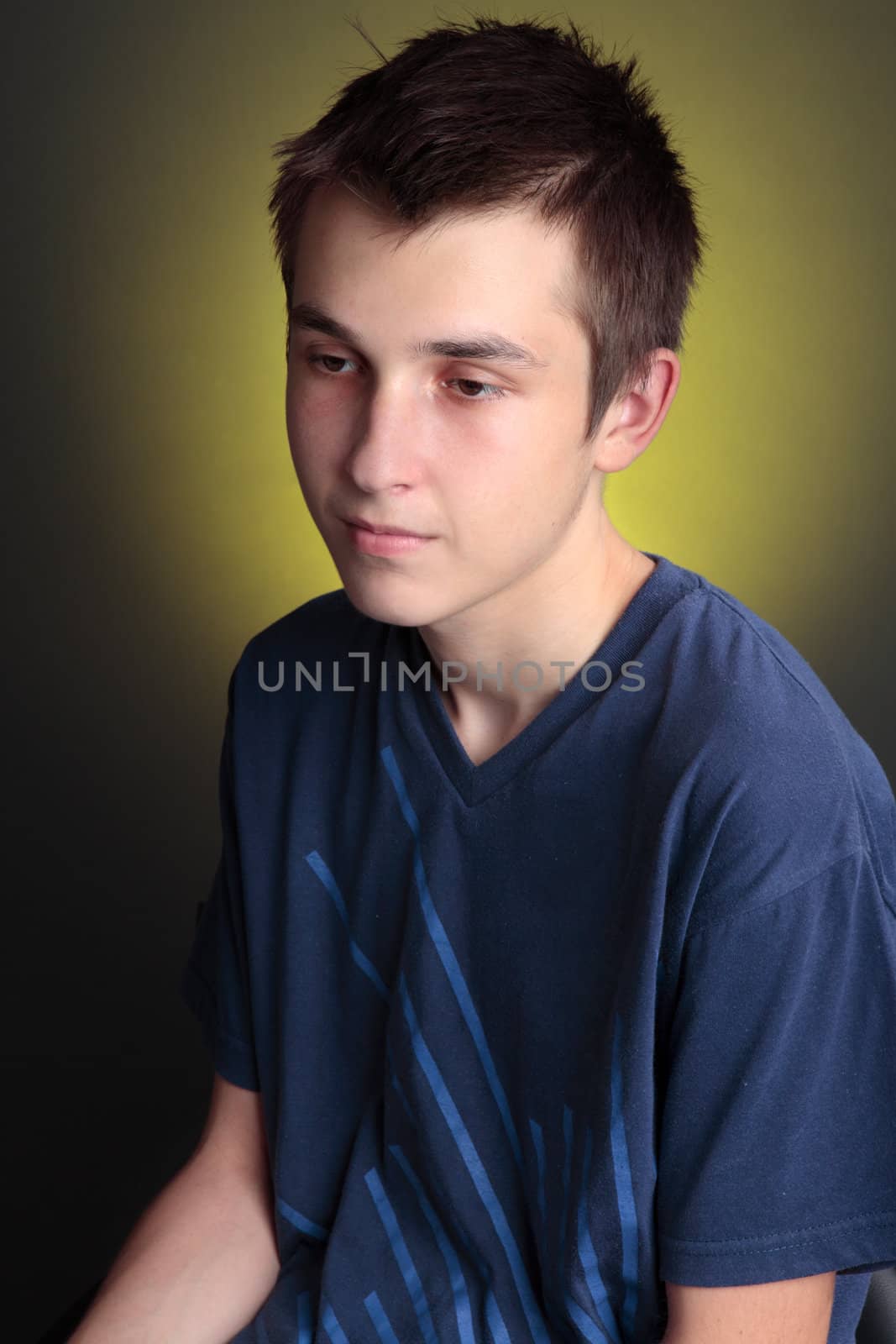 A boy sitting with a downcast face.  Depression, unhappiness, lonliness, etc