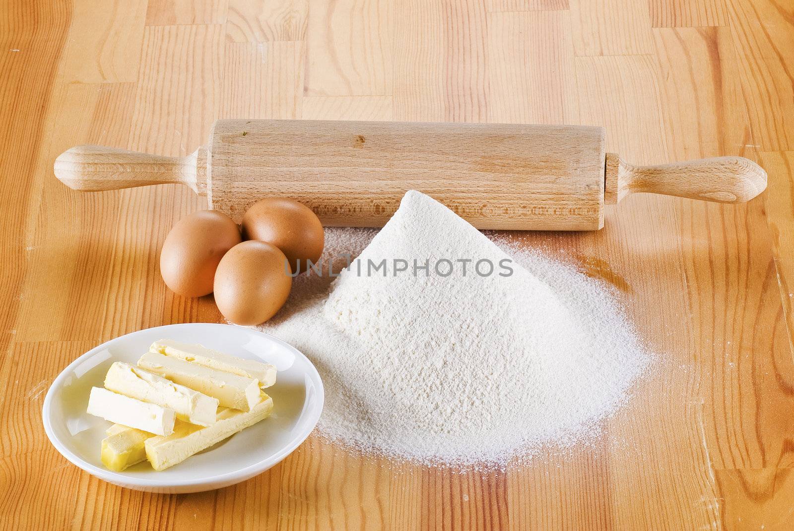 Flour with eggs, rolling pin and butter on the wooden table