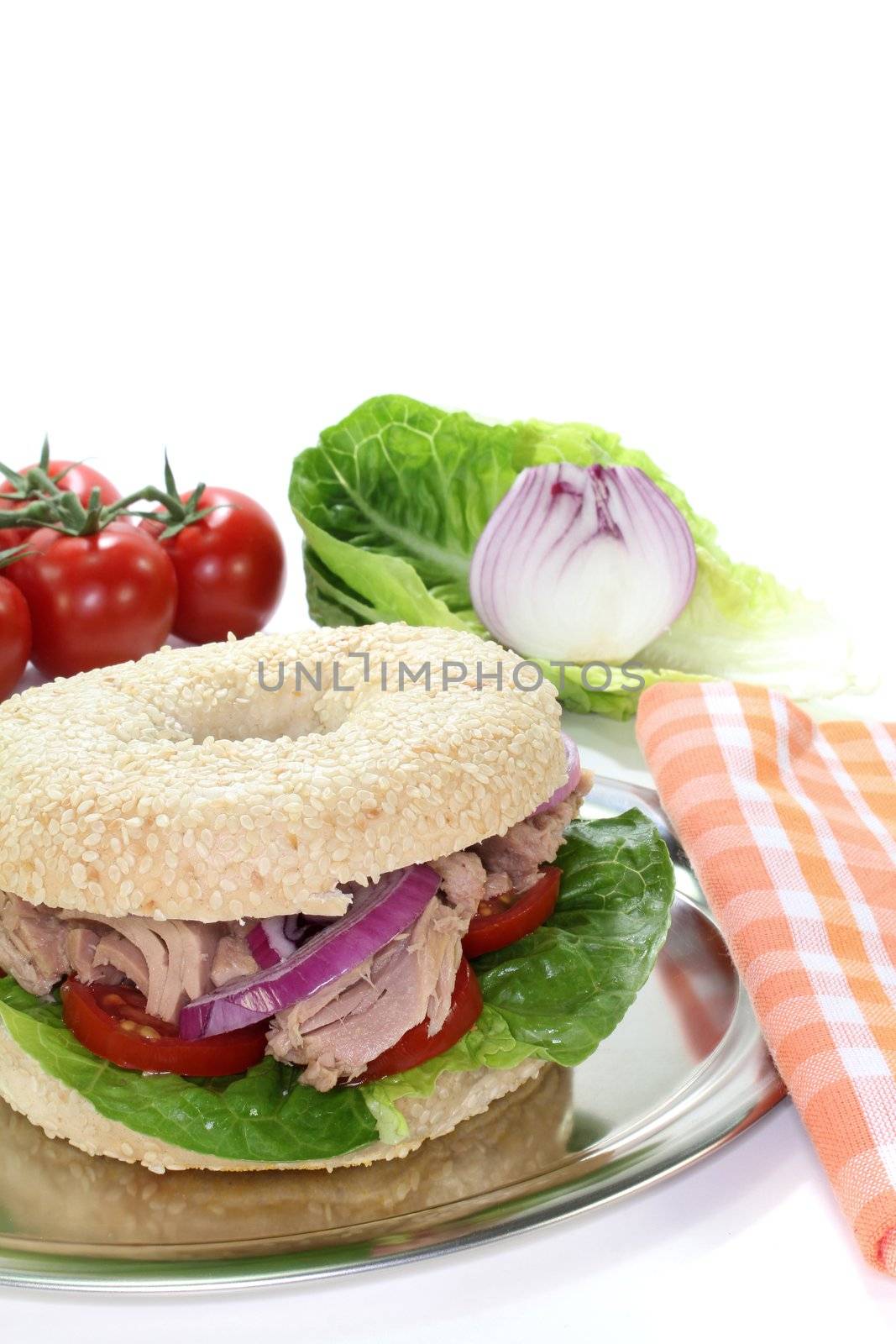 Bagel with tuna, tomatoes, onions, and lettuce on white background