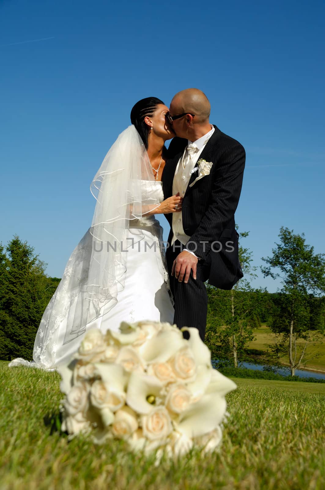 A wedding couple is kissing. The bouquet is in blur