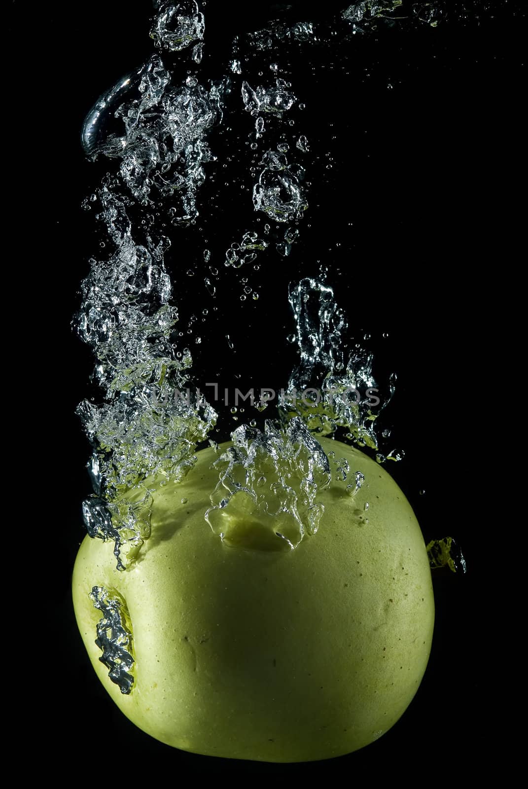 A green apple splashing on a water surface with a black background.