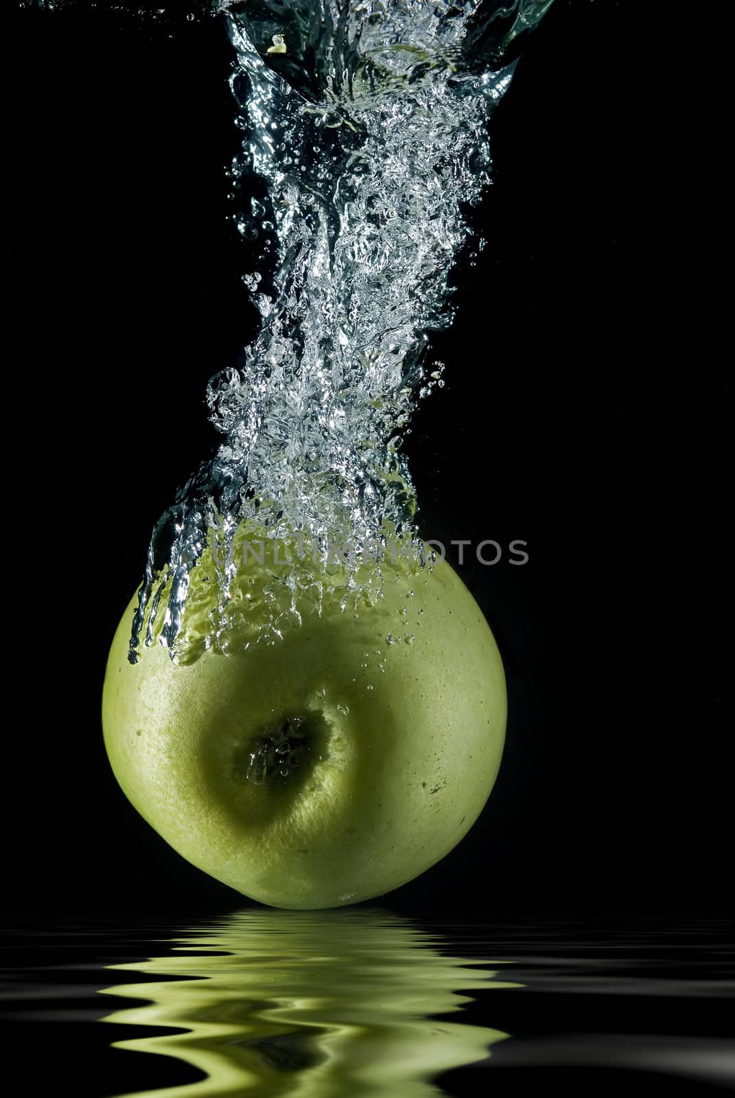 A green apple splashing on a water surface with a black background.