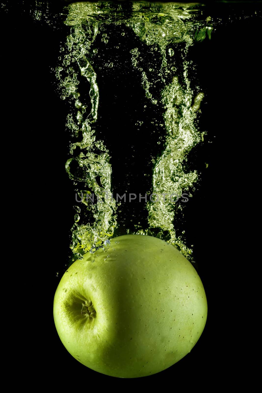 A green apple splashing on a water surface with a black background.