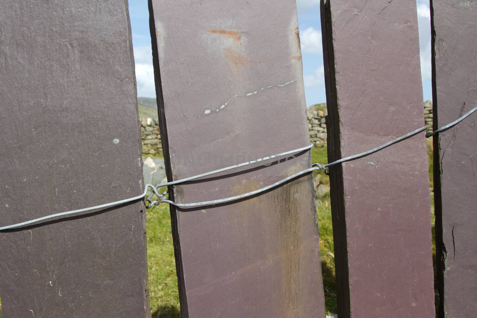 The panels of a slate fence connected with metal wirewith a blue sky in the background.