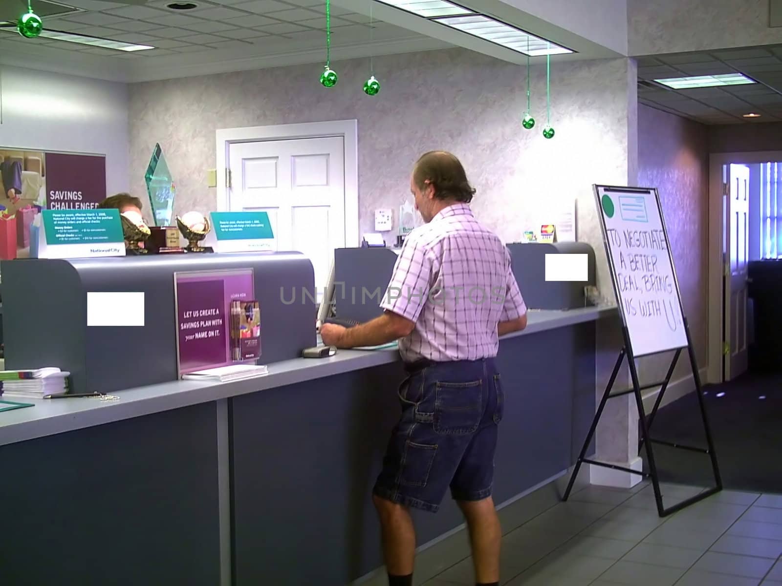 A man is inside a bank for some business, and he is talking to a teller who is standing behind the counter.