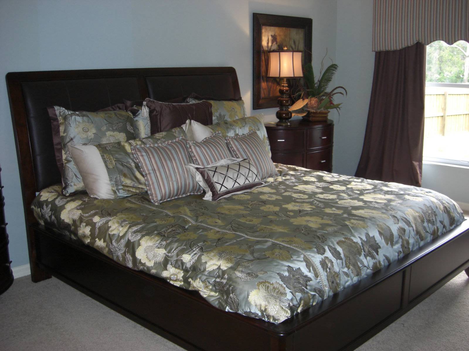An elegant looking  bed is ardoned with silk covers and pillows inside a room that is decorated in a combination of soft blue, brown and beige colors. 