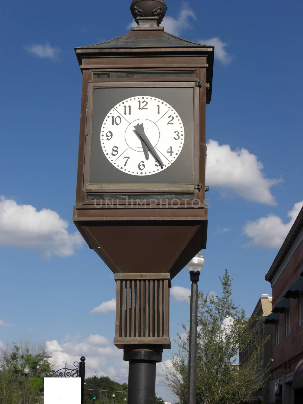 A big clock is standing tall on the side of a street in a city center.