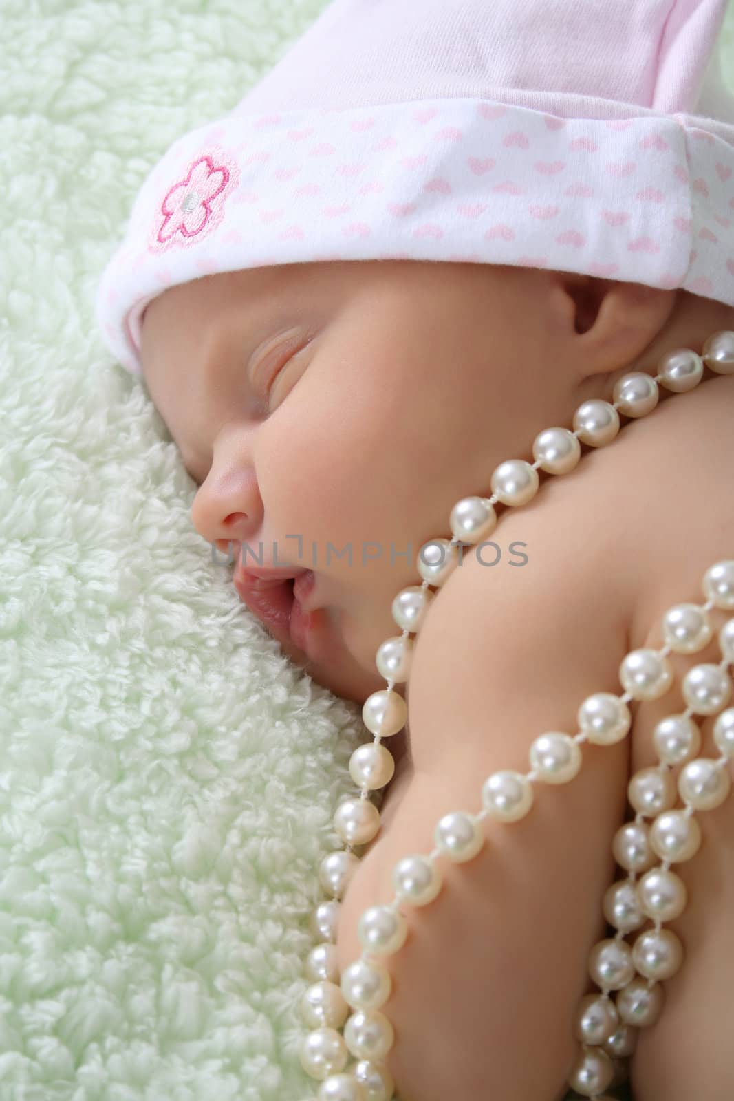 Beautiful newborn baby girl sleeping on a fluffy blanket with pearls draped