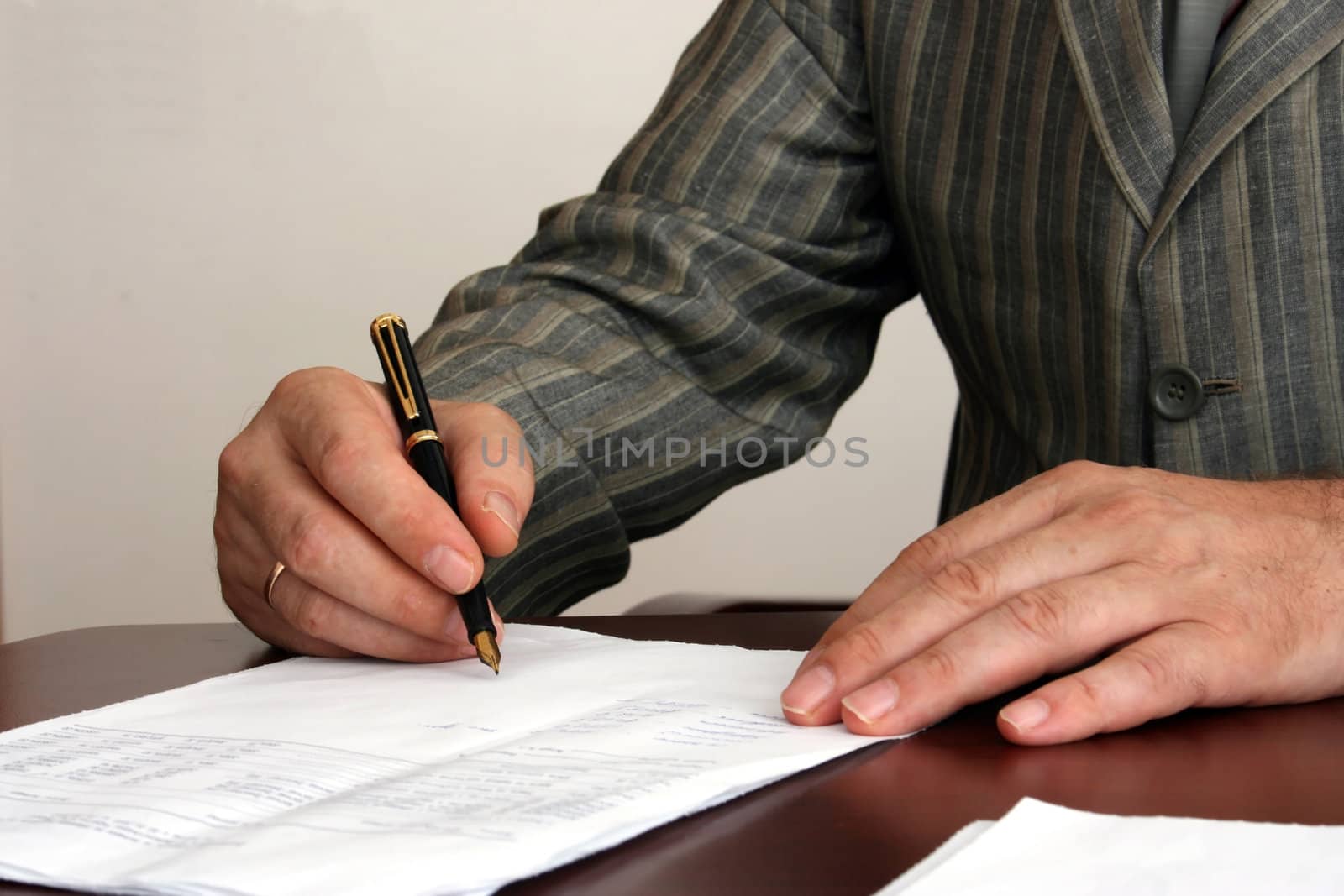 The man in a striped jacket signs the document. In a picture the hand with pen and a sheet of paper on a table is visible