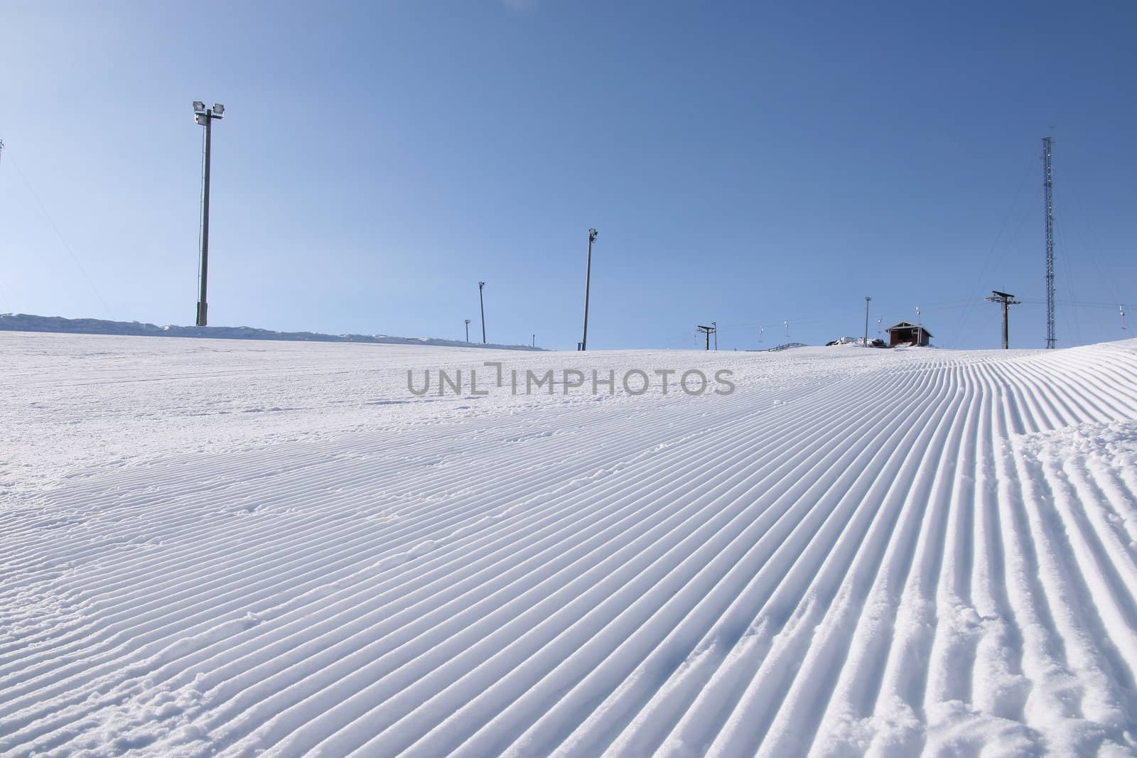 A newly groomed skislope under a clear blue sky