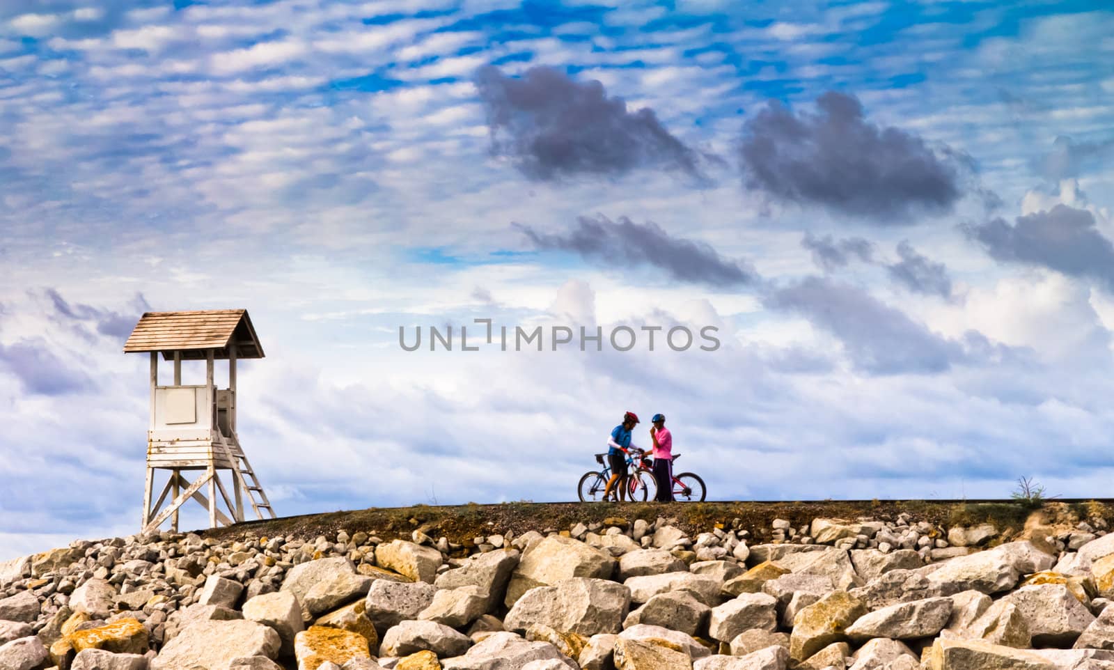 Men are towed bicycle and lighthouse at sunset.