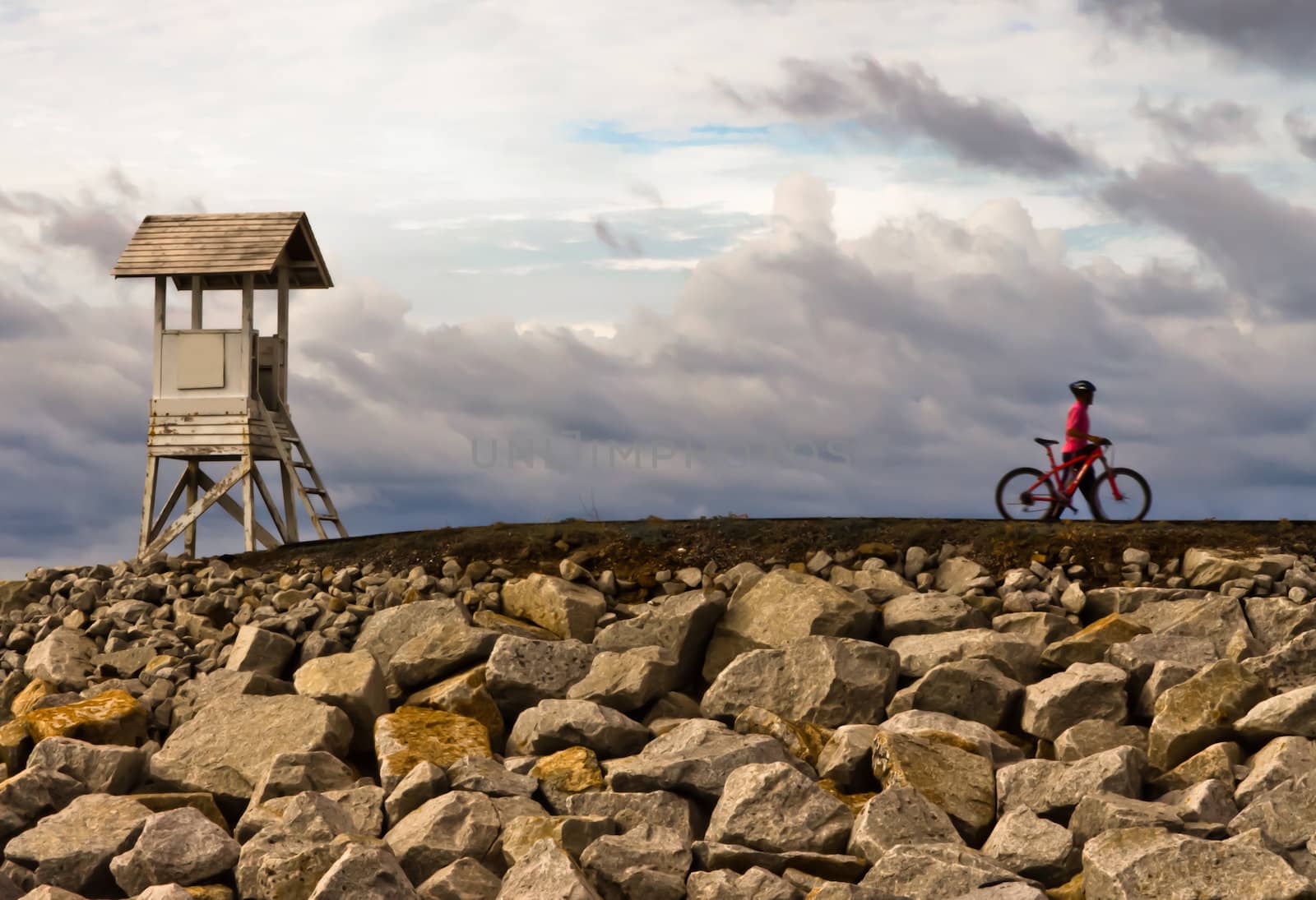 Men are towed bicycle and lighthouse at sunset.