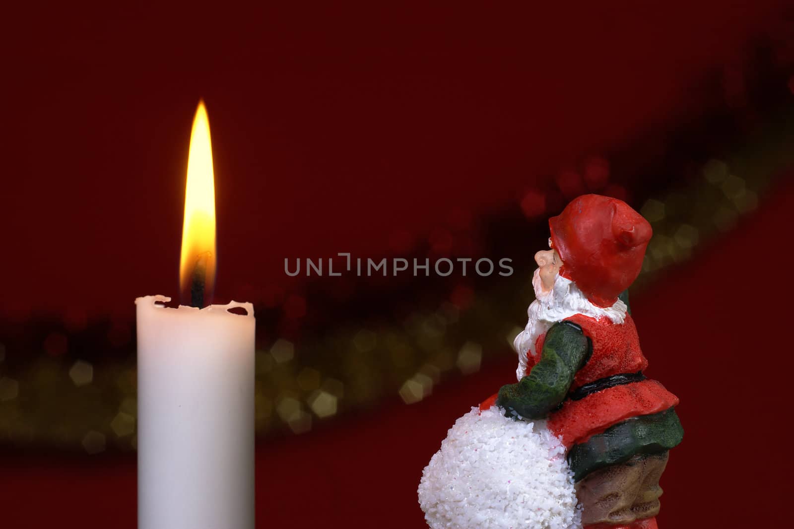 A small santa looking at a lit candle