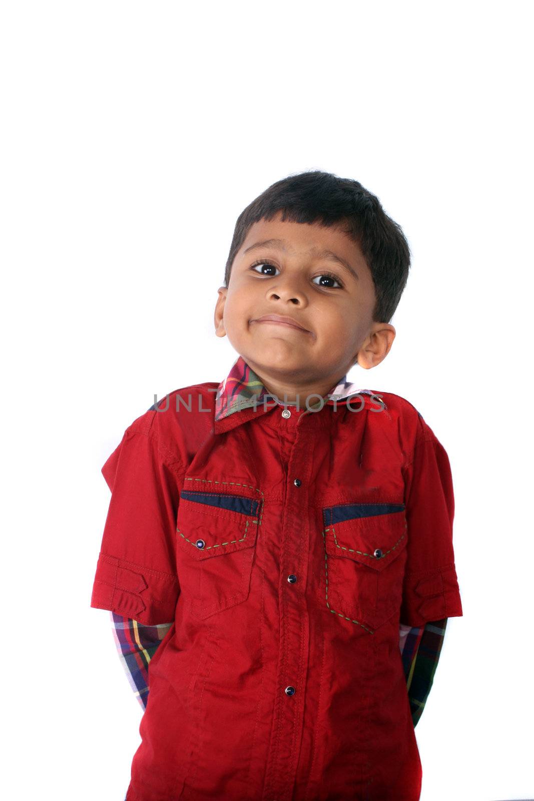 A cute Indian boy pretending to be innocent after playing a mischief, isolated on white studio background.