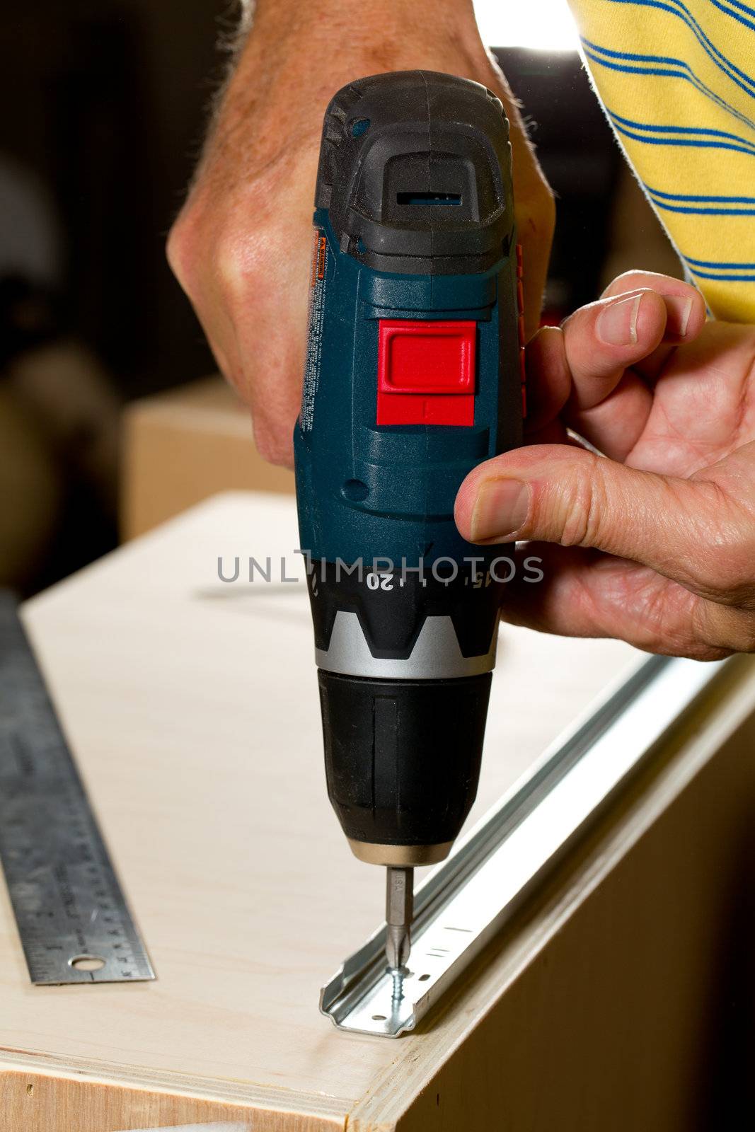 Screwing a screw into a drawer runner on side of wooden drawer using a battery drill