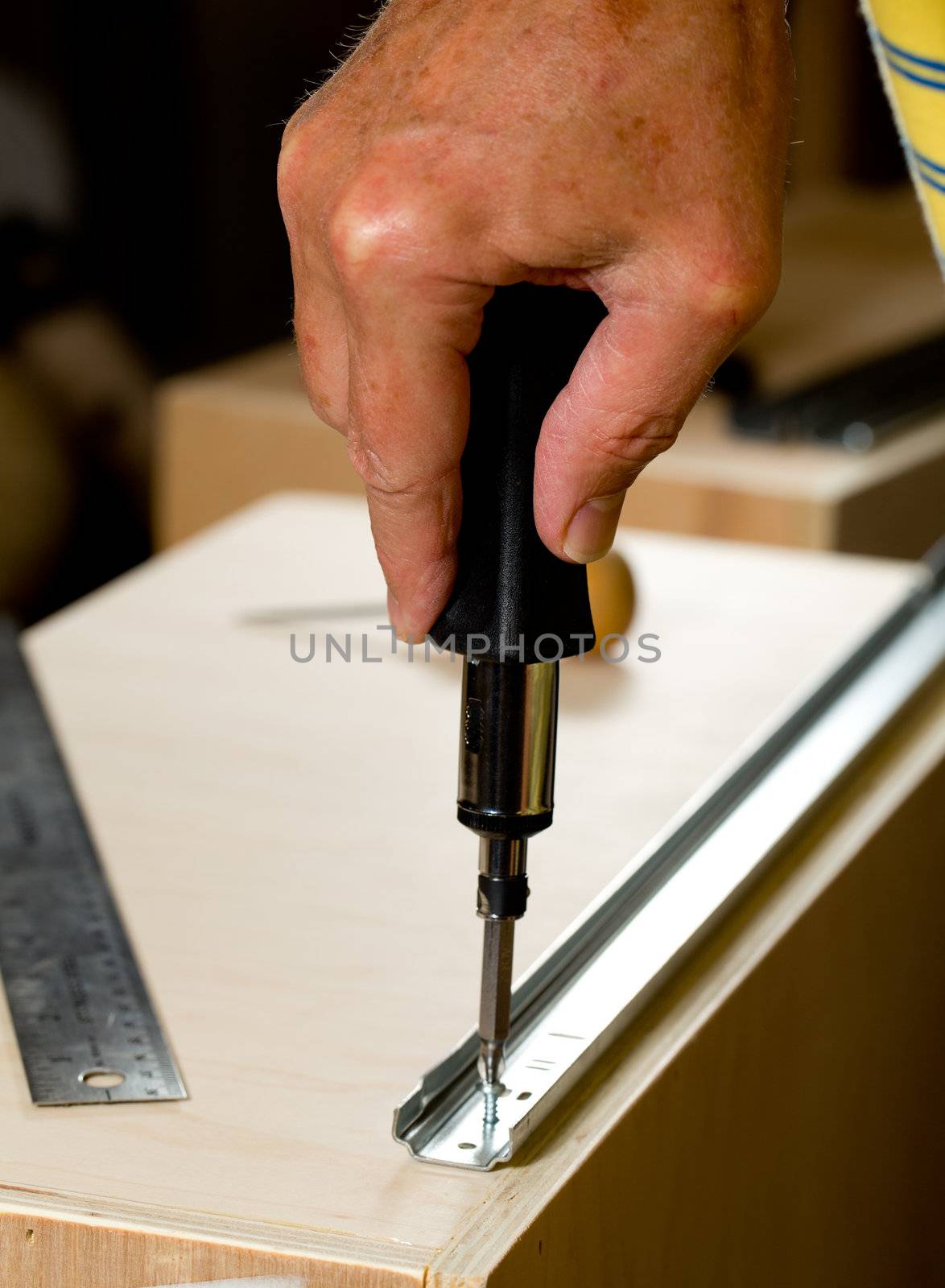 Screwing a screw into a drawer runner on side of wooden drawer