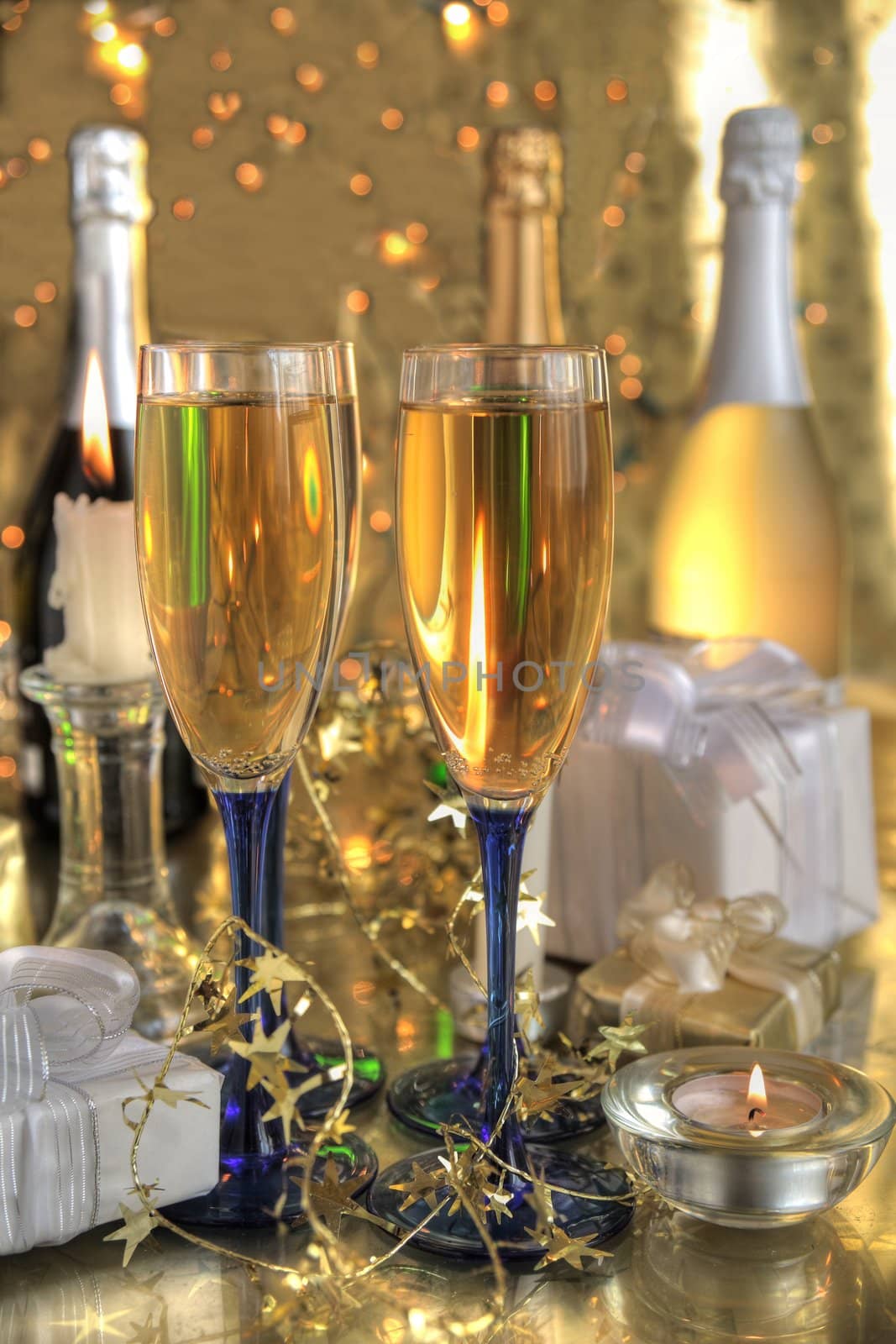 Champagne in glasses,bottles,gifts,candle light and blurred lights on gold background