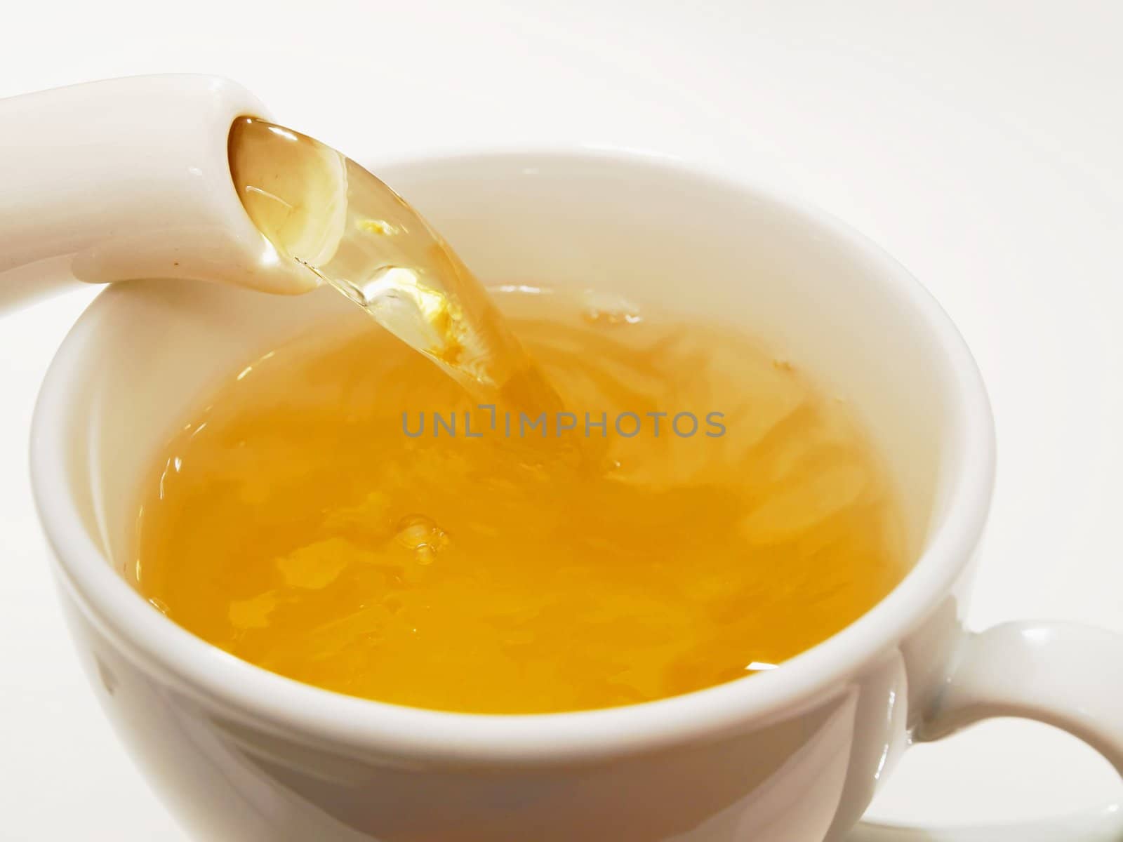 Tea coming out from a mug into a little cop towards white background