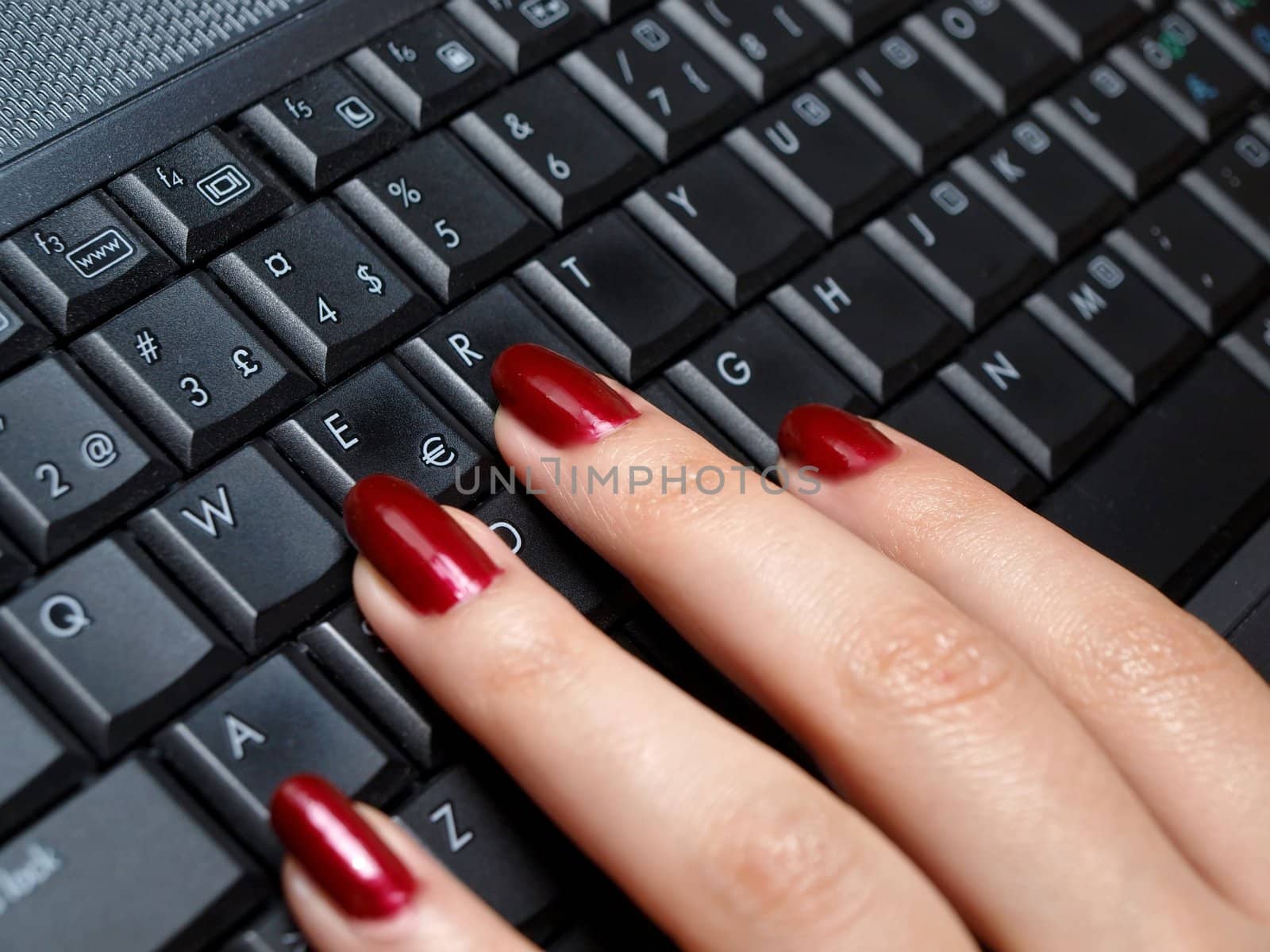 Woman typing on a keyboard with fresh manicure, red color. 