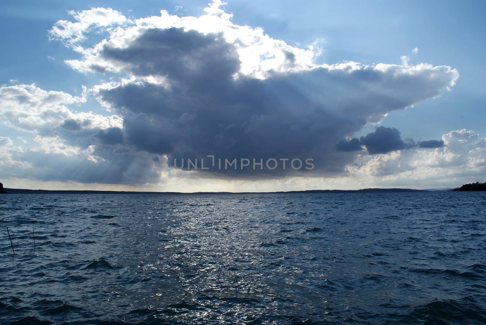 A dark cloud of interesting shapes. Behind him, penetrating rays of the sun that shines on the sea.