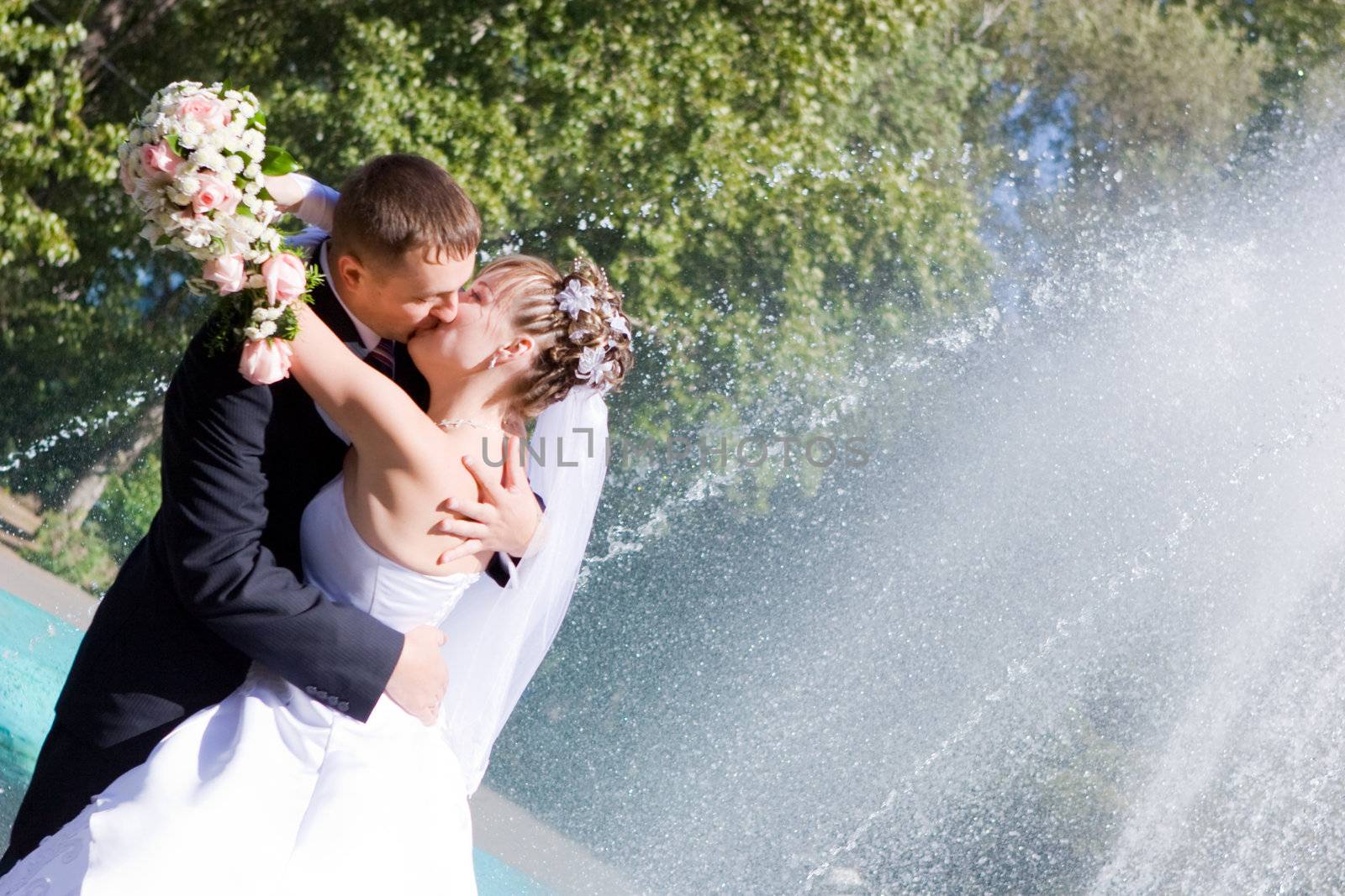 a bride bouquet of flowers and a groom kissing near the fountain