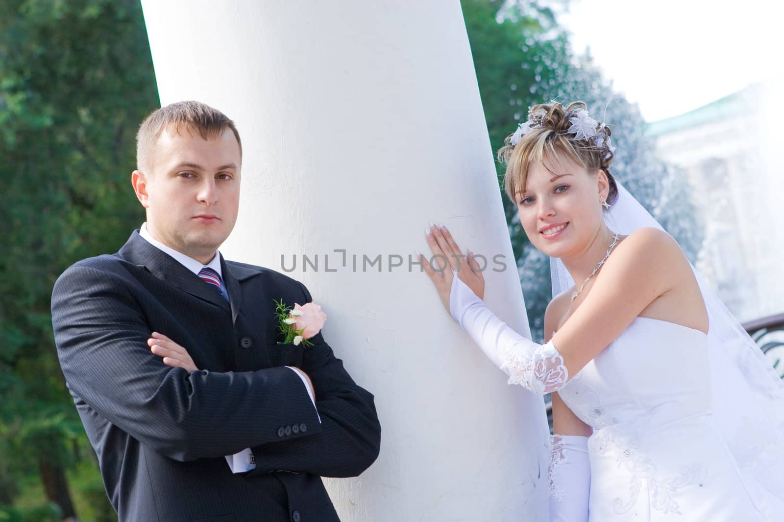 a bride and a groom stand by a white column