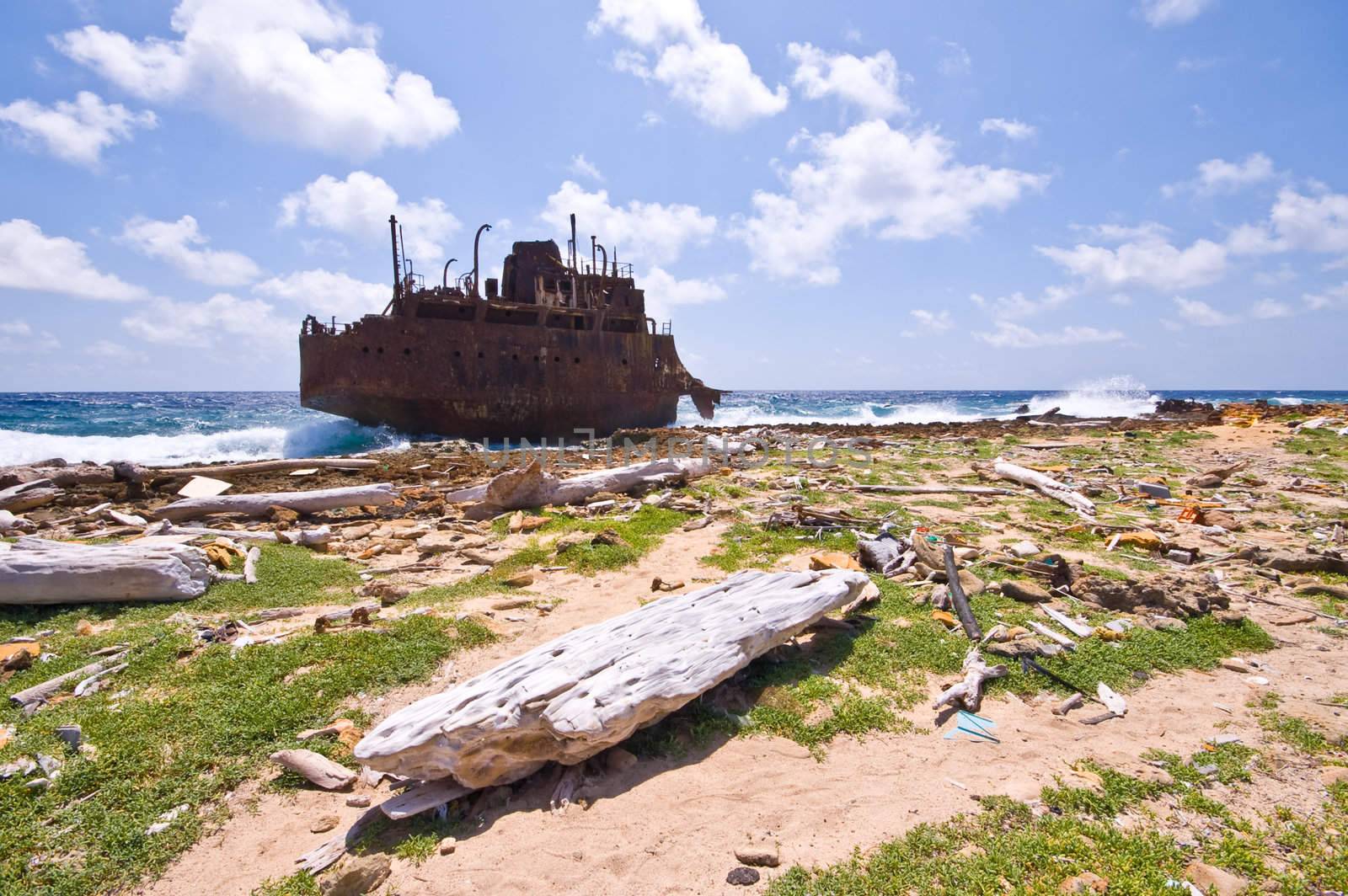 rusty wreck on little curacao with rubbish washed on the shore line