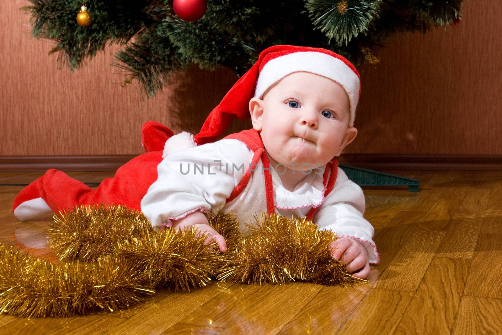 Little baby as Santa in red cap laying on the floor with gifts