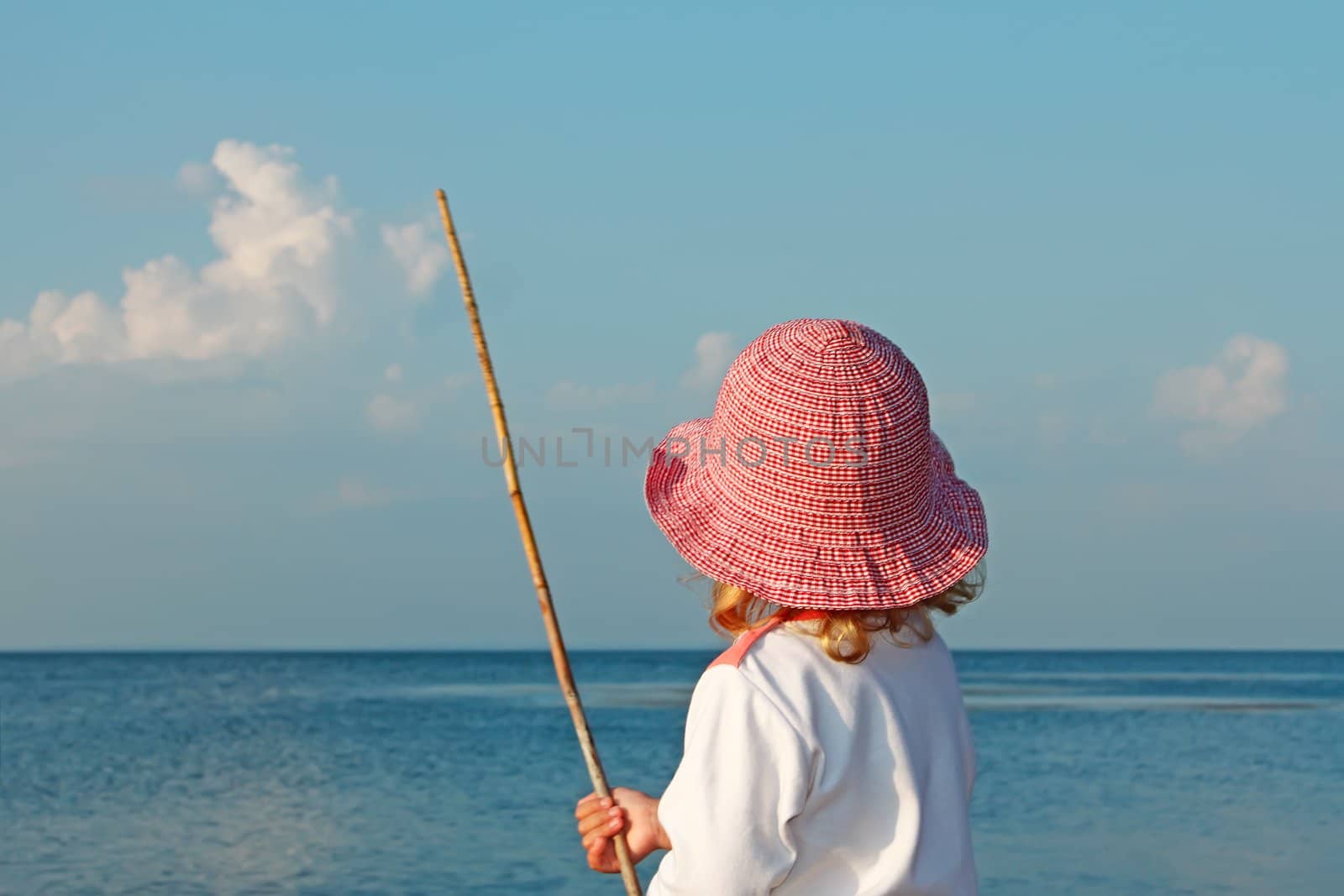 A little girl in a red bonnet with a stick in his hands on the seashore
