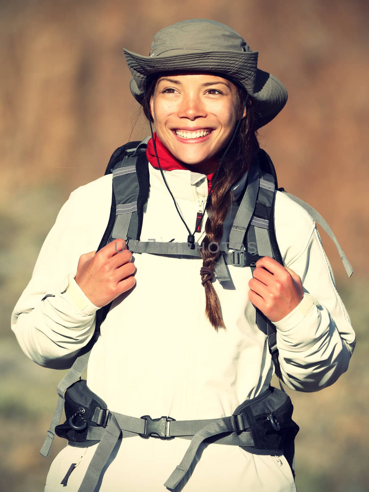 Hiker woman happy smiling outdoors while hiking in autumn or spring sporty outfit. Beautiful fresh Caucasian / Asian female model in warm evening light.