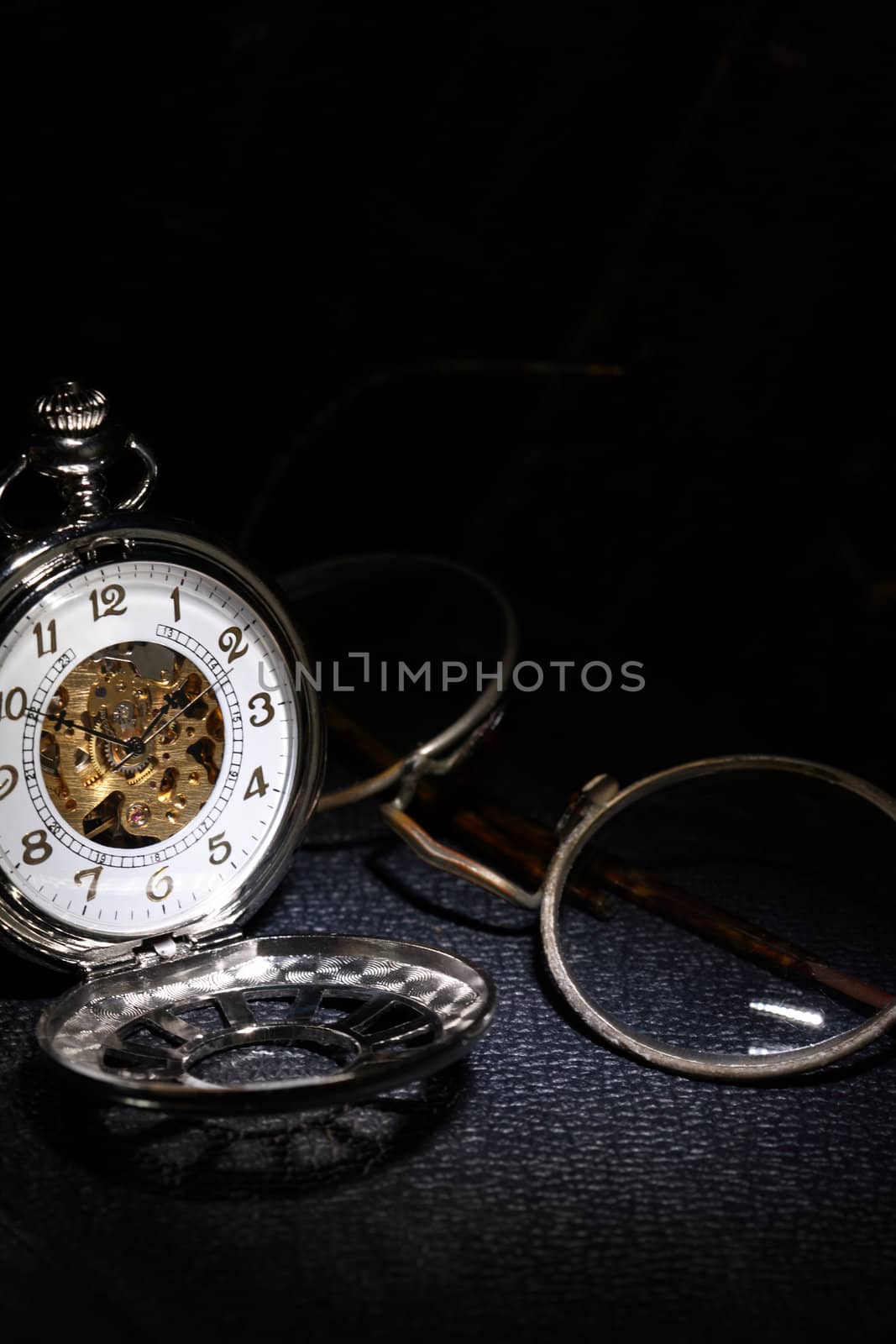 Closeup of vintage pocket watch near spectacles on dark background