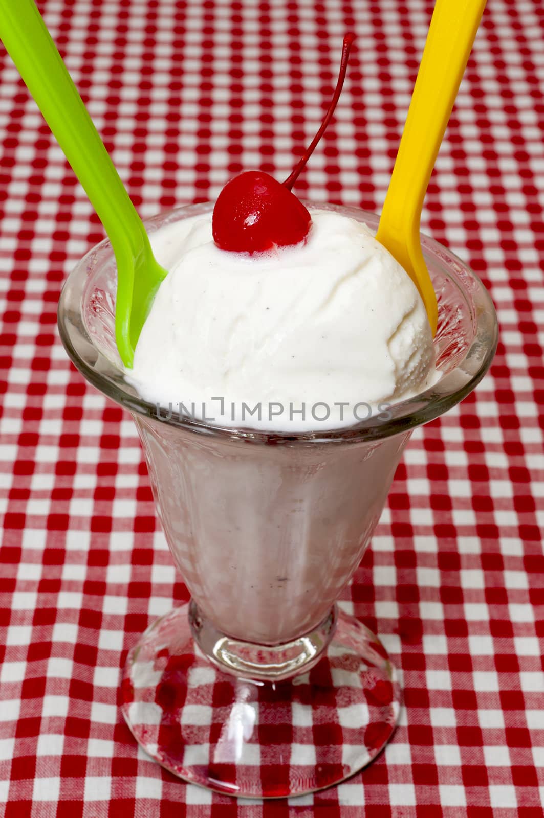 Vanilla ice cream and spoons with cherry topping on table with red gingham table cloth.