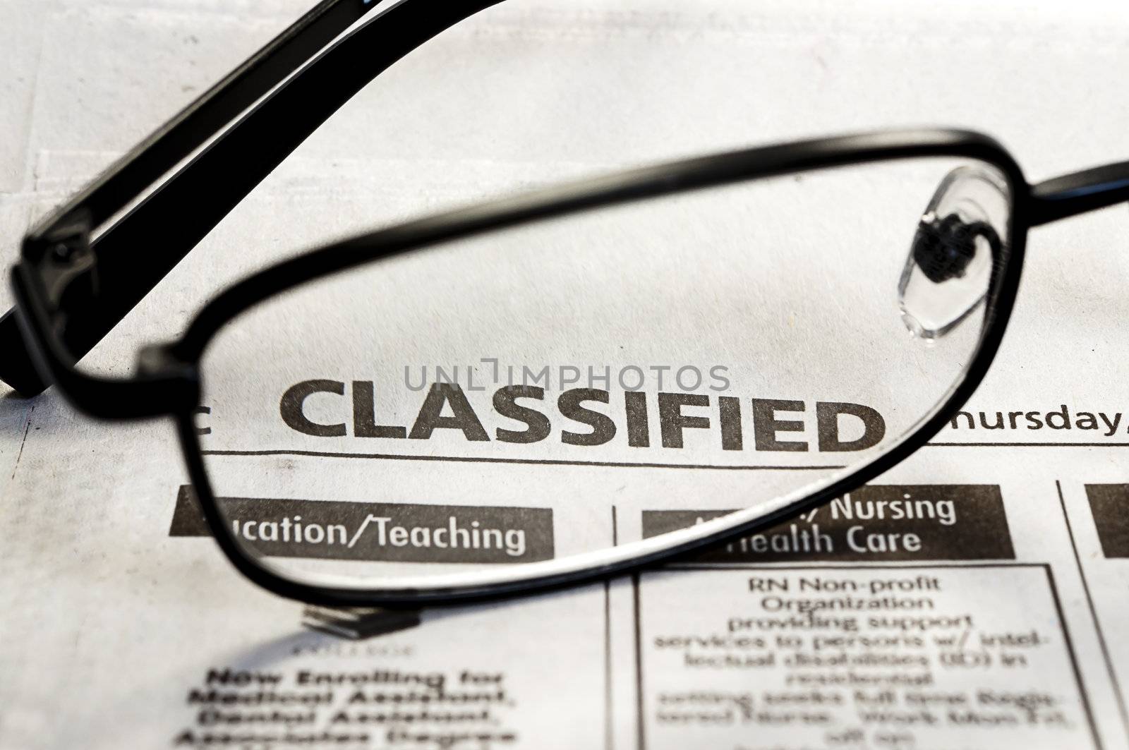 Closeup of classified ads in newspaper with reading glasses.