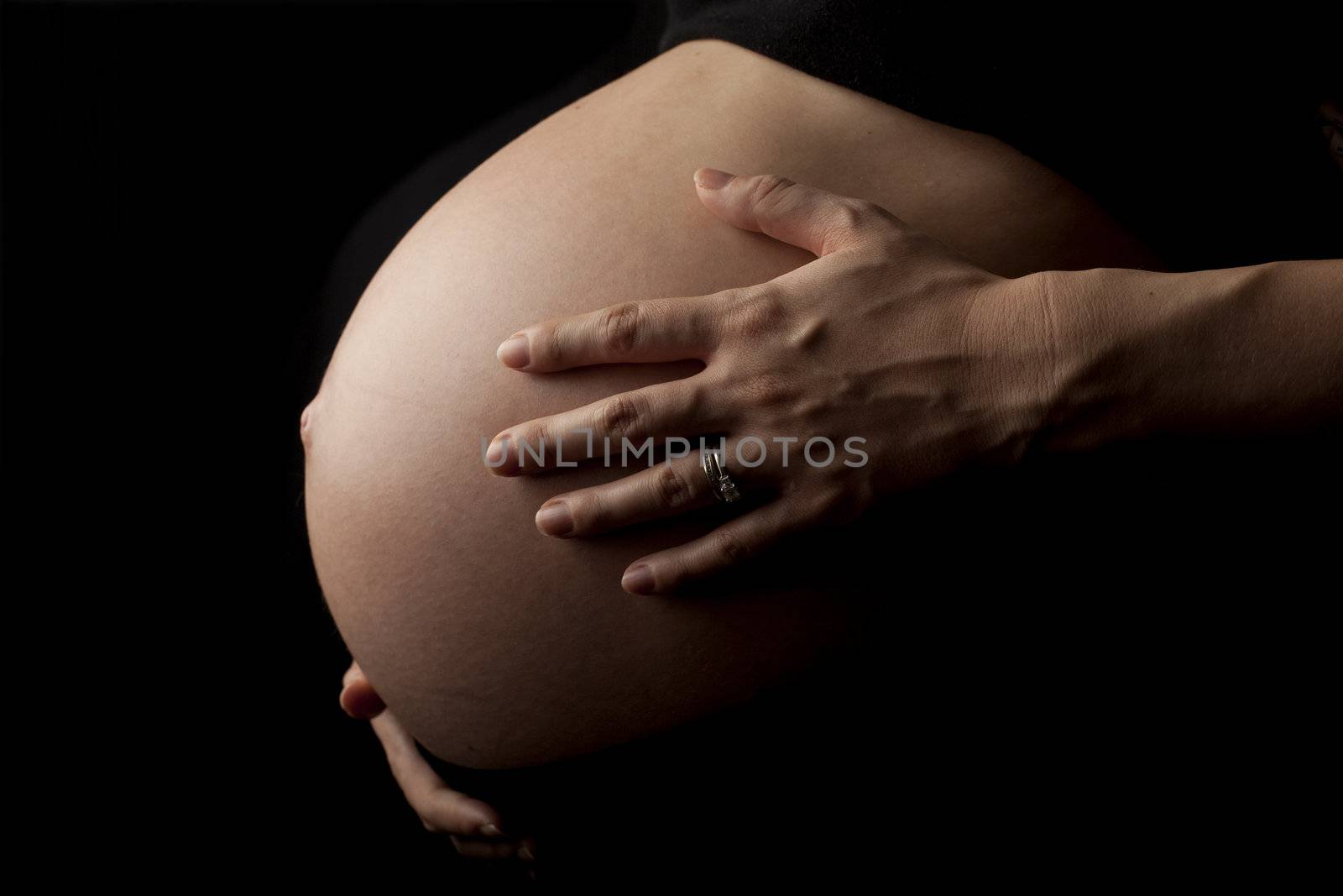 close up of a pregnant womans stomach, isolated on black background.