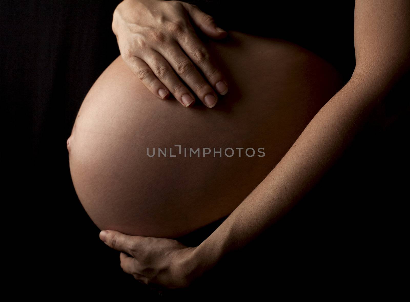close up of a pregnant womans stomach, isolated on black background.