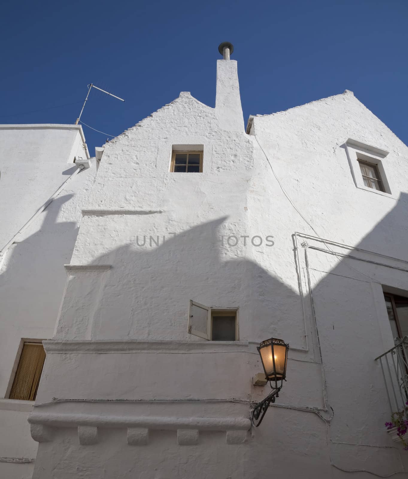 White painted fcade with lamp and shadow againt a nice blue September sky - Martina Franca, Apulia - Italy.