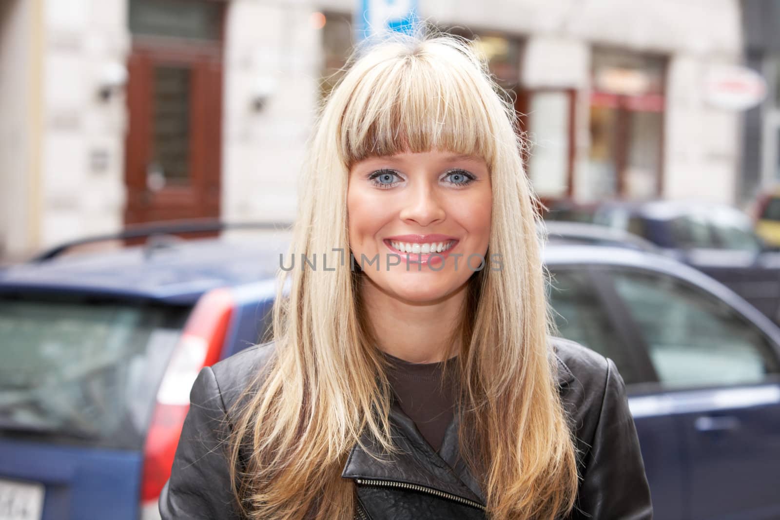 Young woman standing on sidewalk in city, looking at camera, smiling