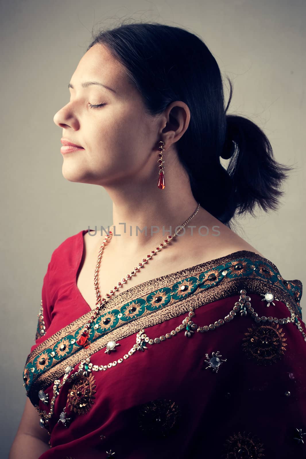 Indian woman stands, relaxed with her eyes closed in beautiful red sari