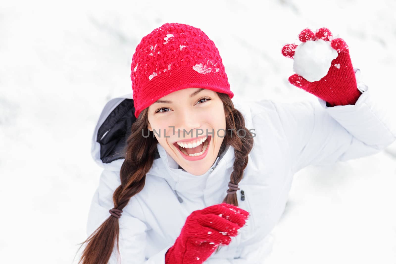 winter girl throwing snowball at camera smiling happy having fun outdoors on snowing winter day playing in snow. Cute playful multicultural Asian Caucasian young woman outdoor enjoying first snow.