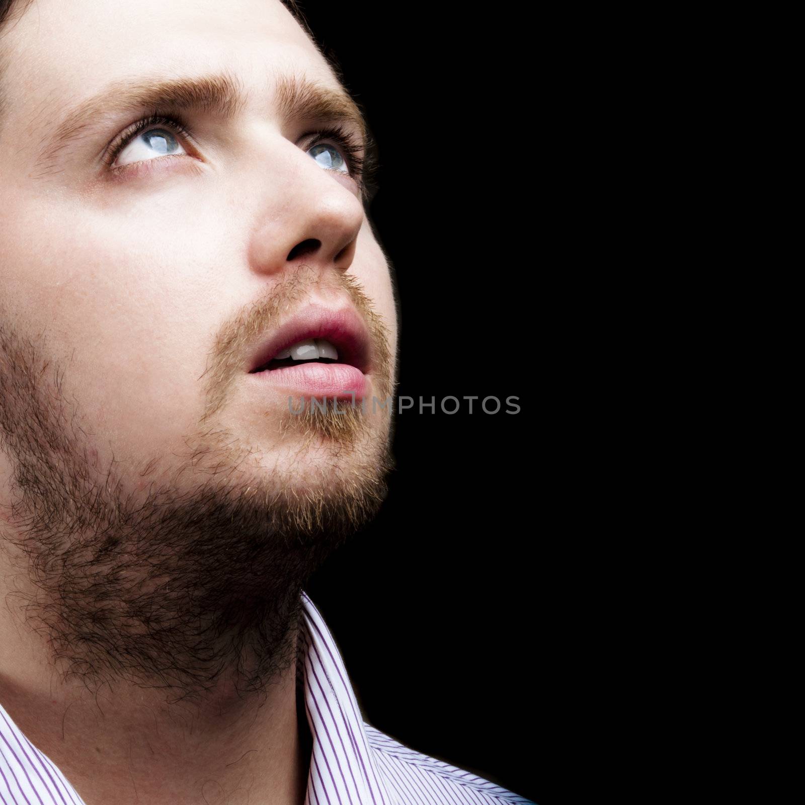 Portrait of a blonde young man gazing upwards to the light on black