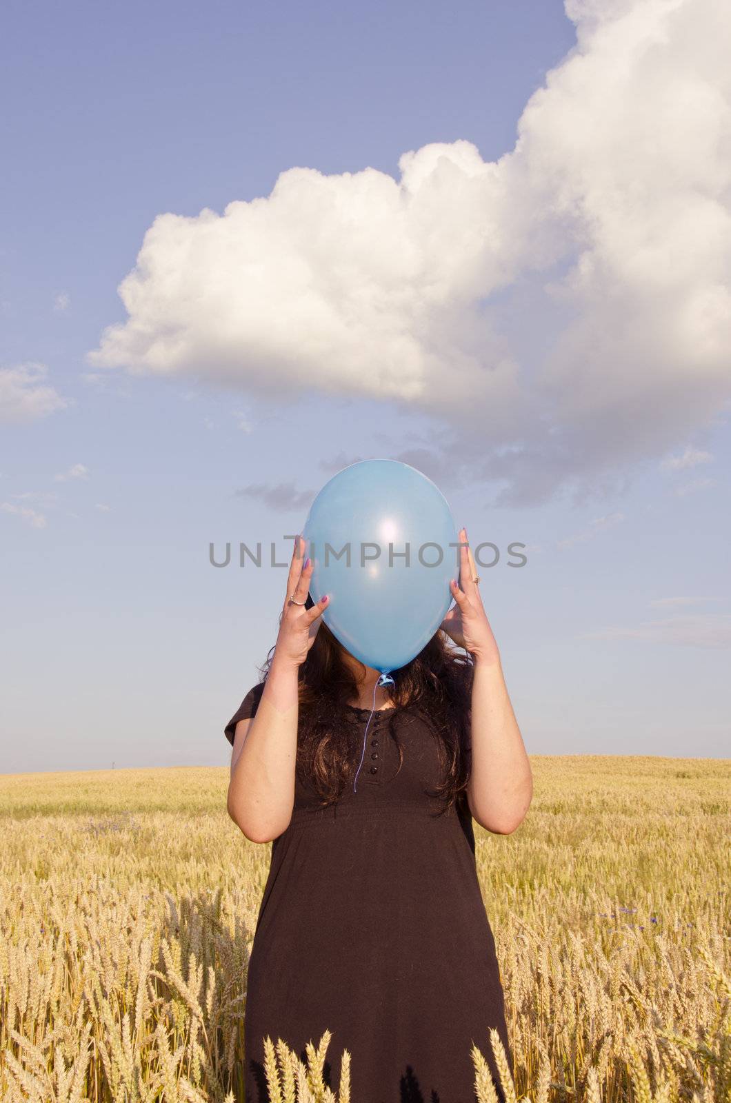 Young woman, dressed with black dress, holding blue balloon in front of her face.