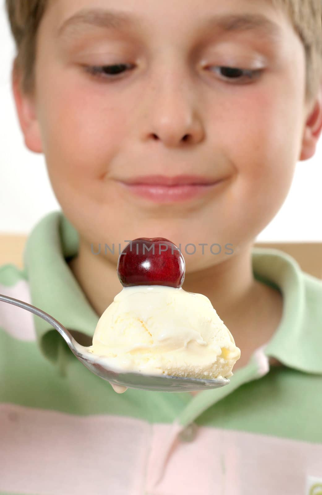 Boy scooping up and holding a spoonful of creamy ice cream with a cherry on top.  Selective focus.