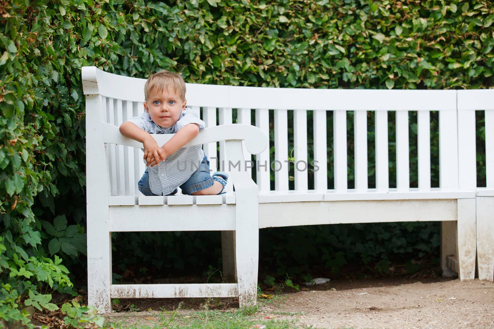 Cute little boy sits on a bench in a park